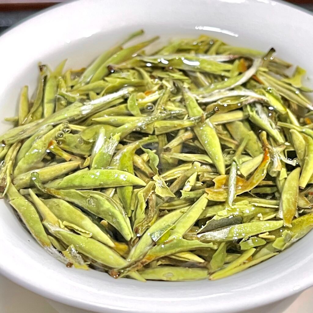Silver Needle white tea — single buds standing upright in a glass cup, showing the silvery down.