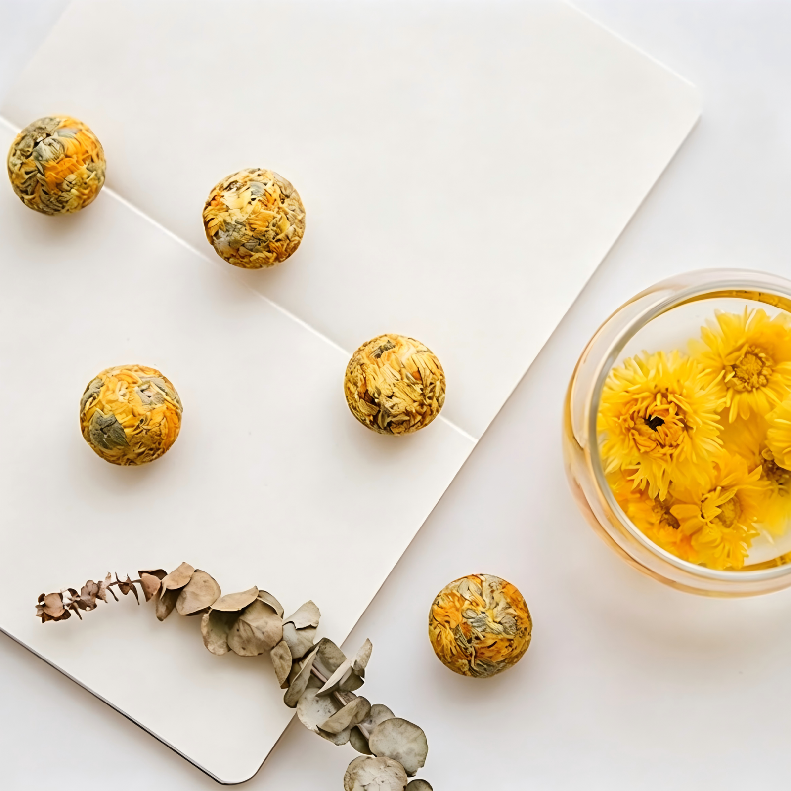 A single Golden Silk Chrysanthemum tea dragon ball unfurling into a large yellow blossom in a glass teapot.