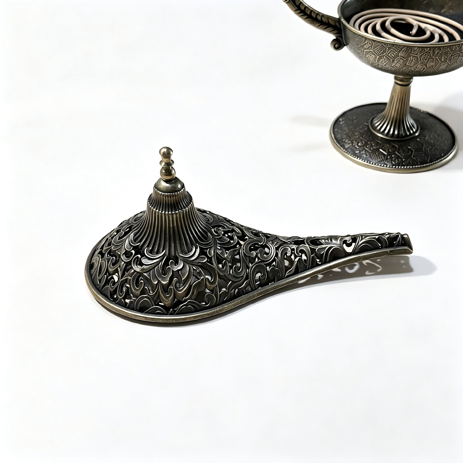 An overhead exploded view of the antique bronze Aladdin lamp incense burner, showcasing the open ash basin layered with fine black incense sand, the detached intricate filigree lid, and a natural brown coil incense beneath on a pure white background.
