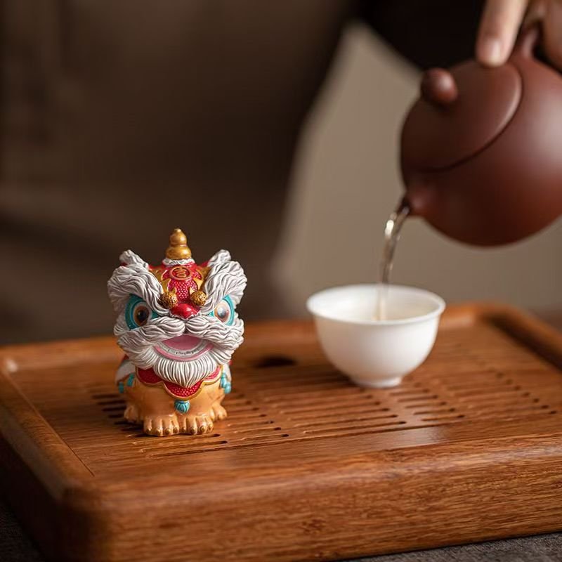 A colorful Chinese tea pet shaped like a traditional lion dance guardian sitting on a bamboo cha pan during a gongfu brewing ritual