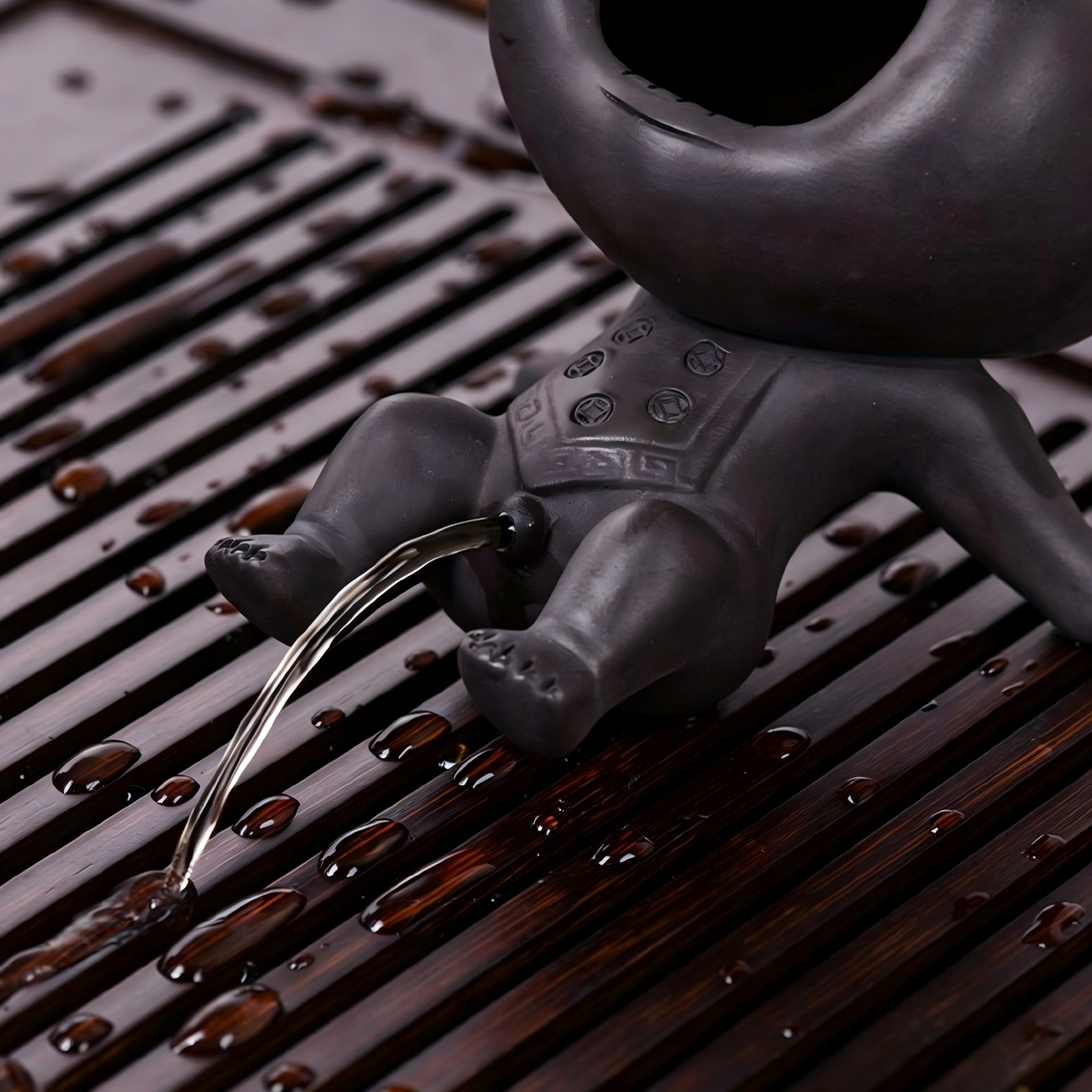 Handcrafted Chinese tea pet made of Zisha clay spitting water on a bamboo tea tray