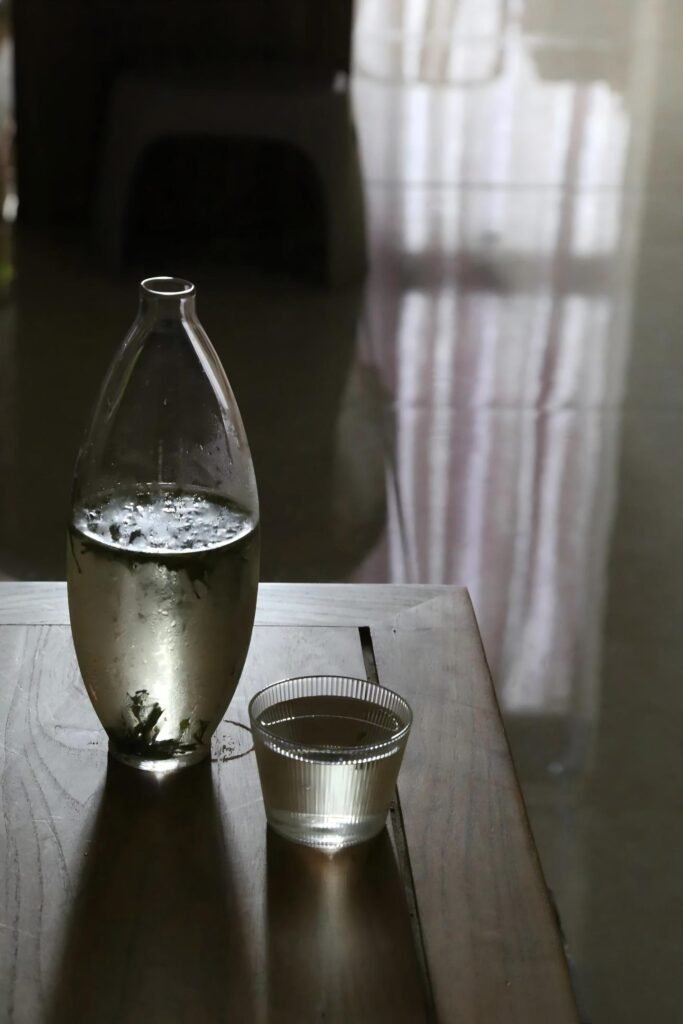 Cold-brewed Longjing green tea in a condensation-covered glass bottle and cup on a wooden table.
