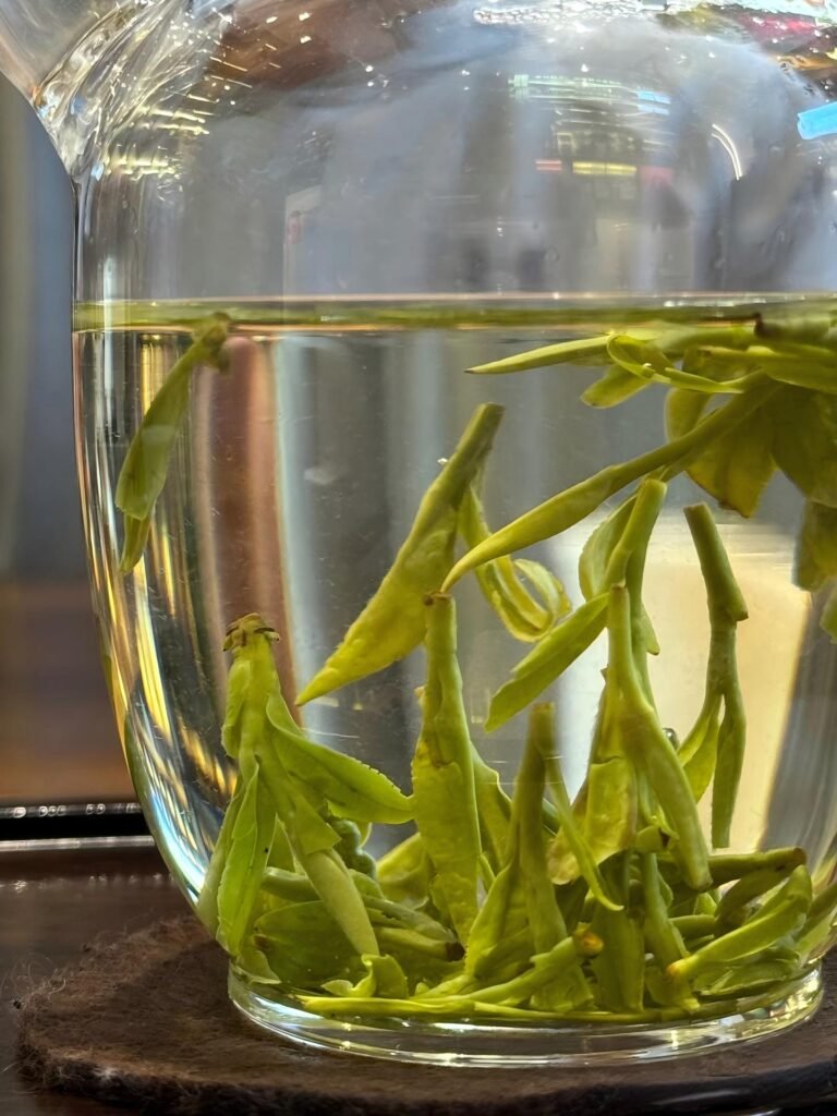Pale jade-green Longjing tea liquor in a tall glass cup]