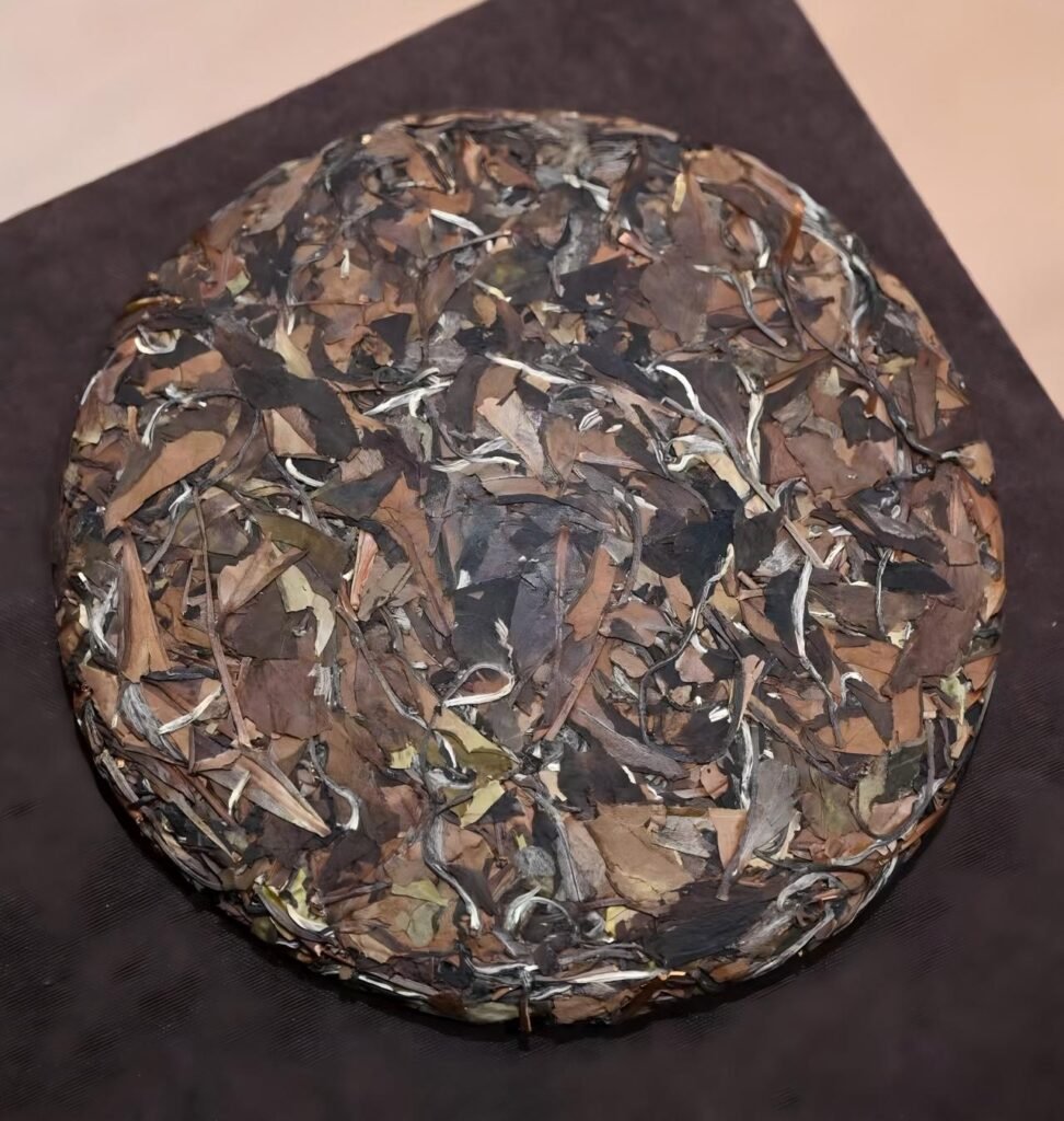 Whole cake of aged Shou-mei white tea wrapped in cotton paper on a wooden shelf.