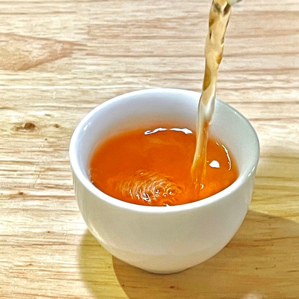 Amber-orange Rou Gui Wuyi rock tea infusion in a white porcelain cup showing thick body and clarity