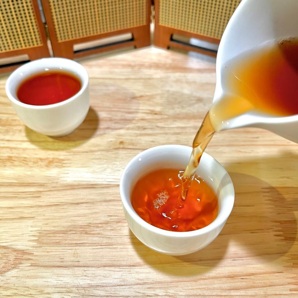 Brewed Zhengyan Yezhuke Rougui oolong tea liquor glowing amber-orange in a glass gaiwan