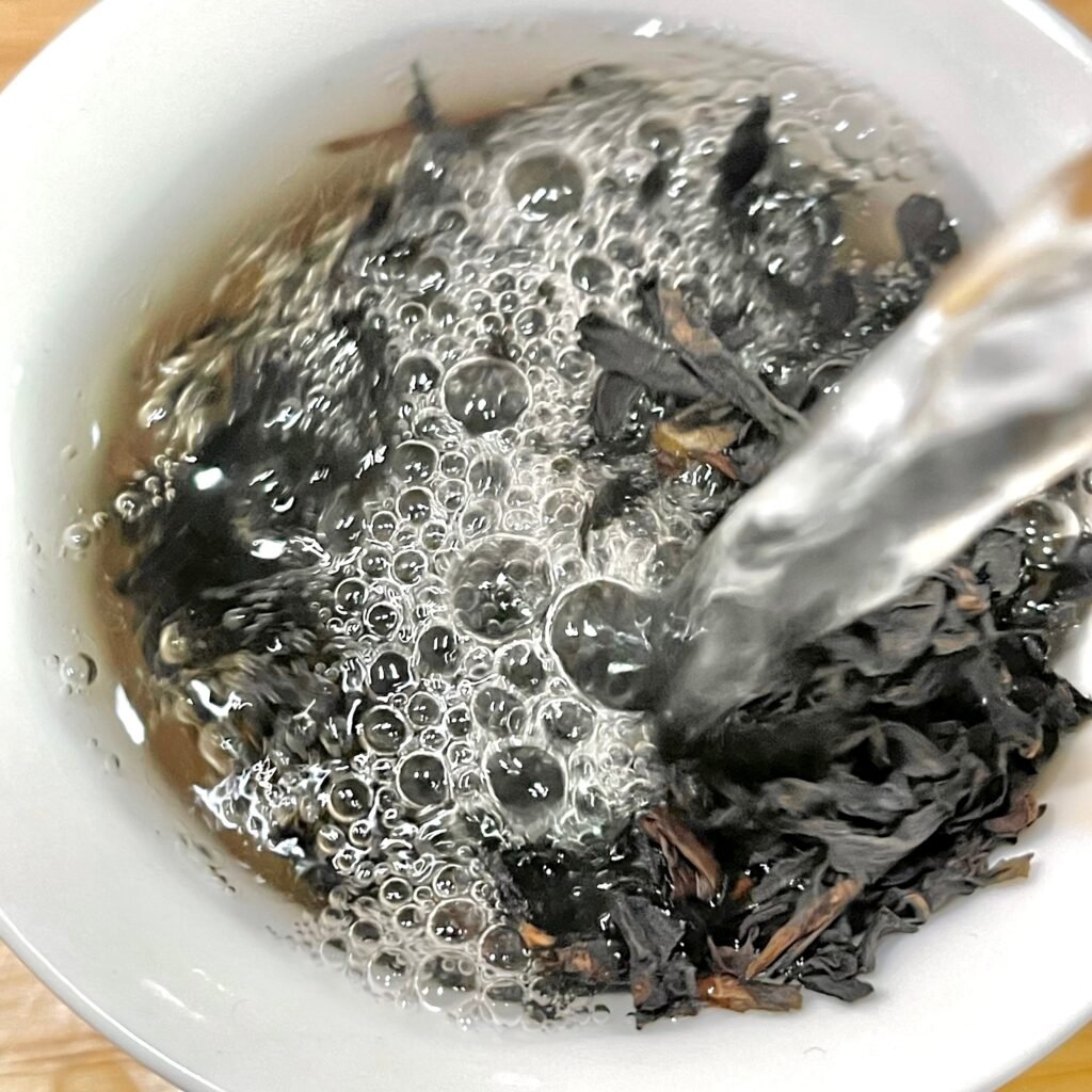 Pouring 100°C boiling water over Wuyi Yancha leaves in a porcelain gaiwan
