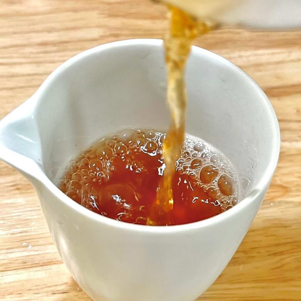 Clear amber first steep of Wuyi Yancha poured from gaiwan into a fairness pitcher